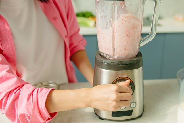 Woman 's hand turning on blender containing a pink smoothie